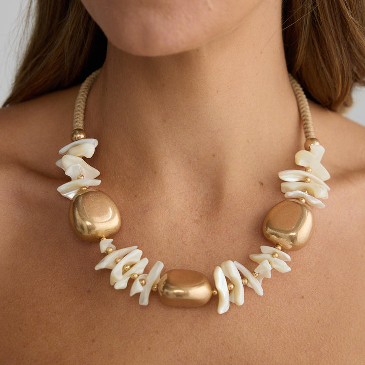 Woman wearing a gold and white beaded necklace against a neutral background