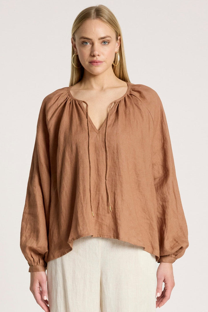 Woman wearing a brown blouse and white pants on a white background