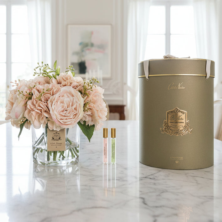 Floral arrangement in a glass vase with two perfume bottles and a decorative box on a white background