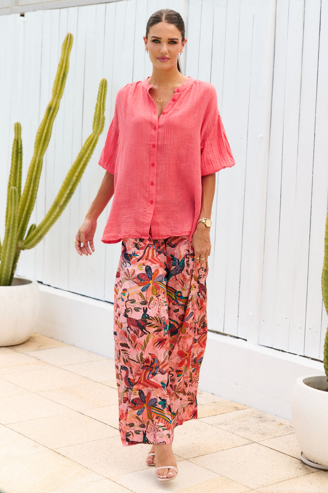 Woman in a pink shirt and floral pants standing outdoors with cacti in the background