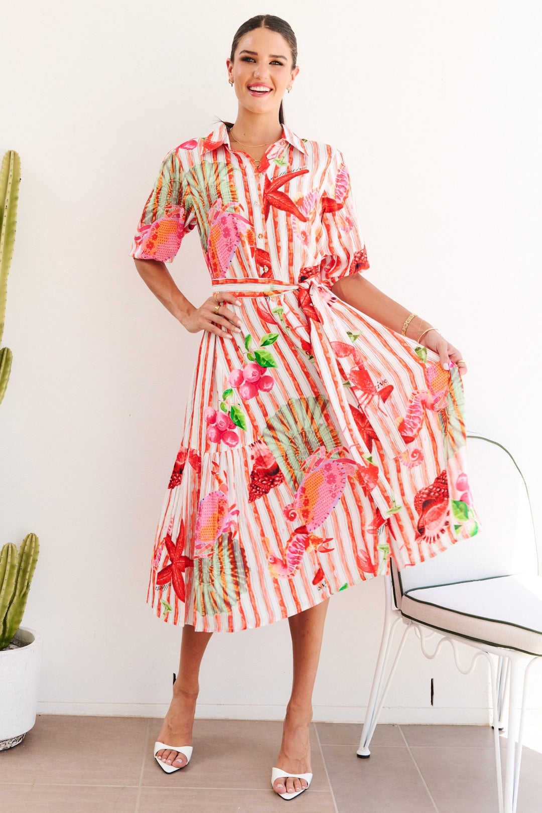 Woman in a colorful dress standing next to a cactus plant indoors.