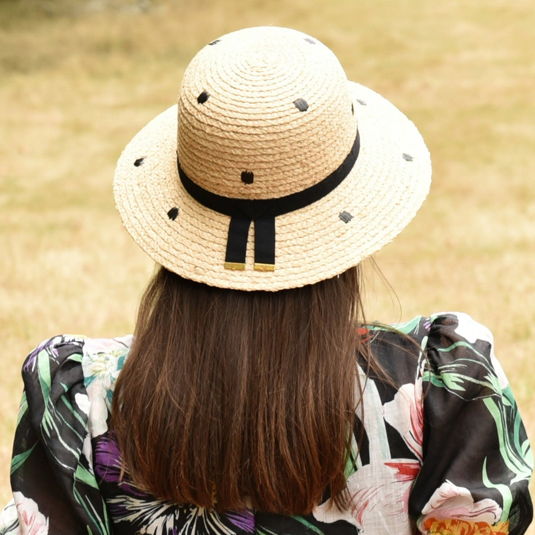 Person wearing a straw hat with a black band and a colorful dress in an outdoor setting.