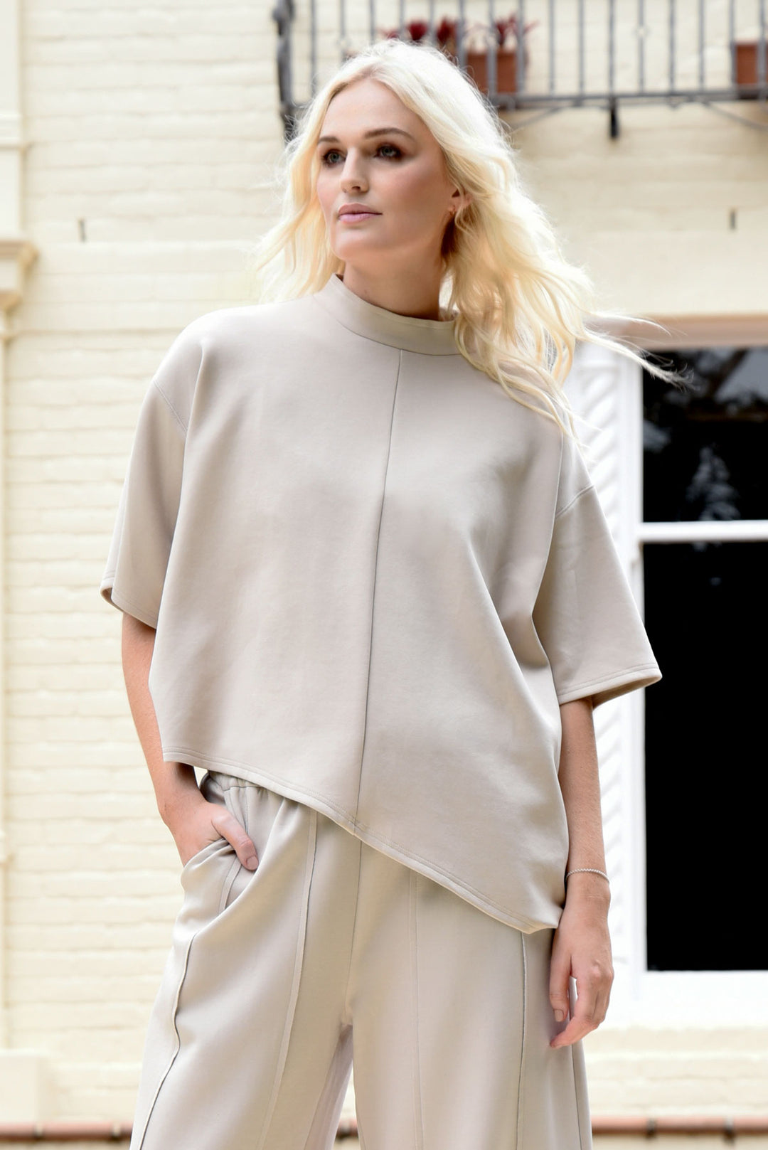woman wearing a lounge top in bone colour in front of a brick home
