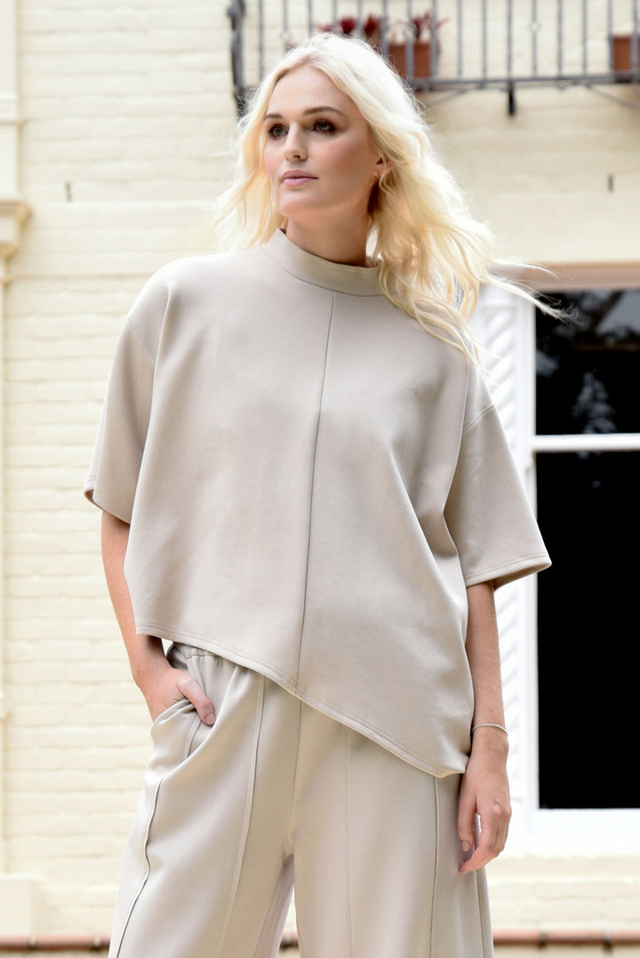 woman wearing a lounge top in bone colour in front of a brick home