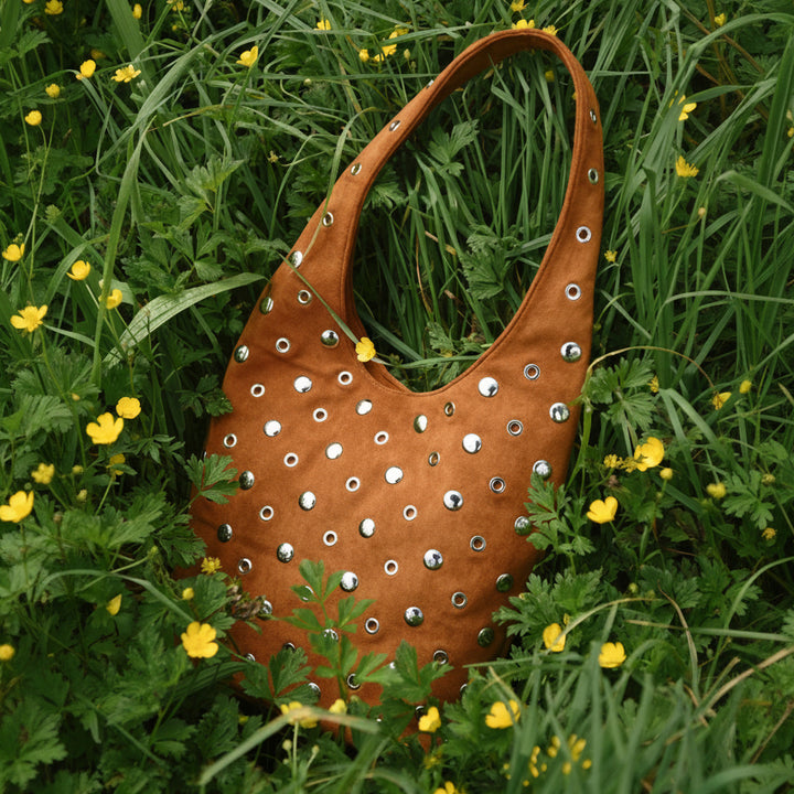 Brown leather handbag with studs on a grassy background with yellow flowers