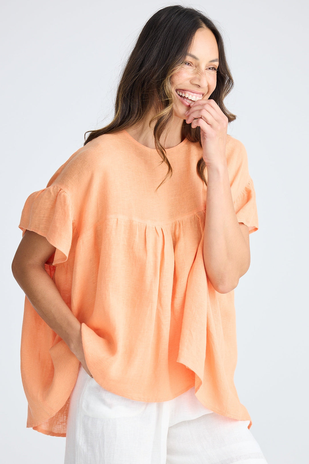 Woman wearing an orange blouse and white shorts on a plain background