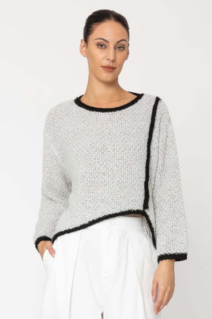 Woman wearing a gray sweater with black trim and white pants on a white background