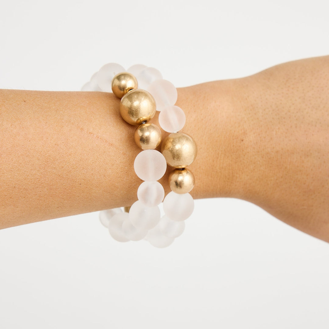 Bracelet with gold and white beads on a wrist against a white background