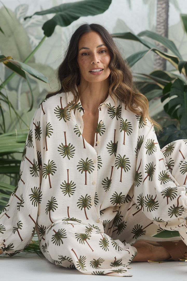 Woman in a white outfit with palm tree pattern sitting among green plants