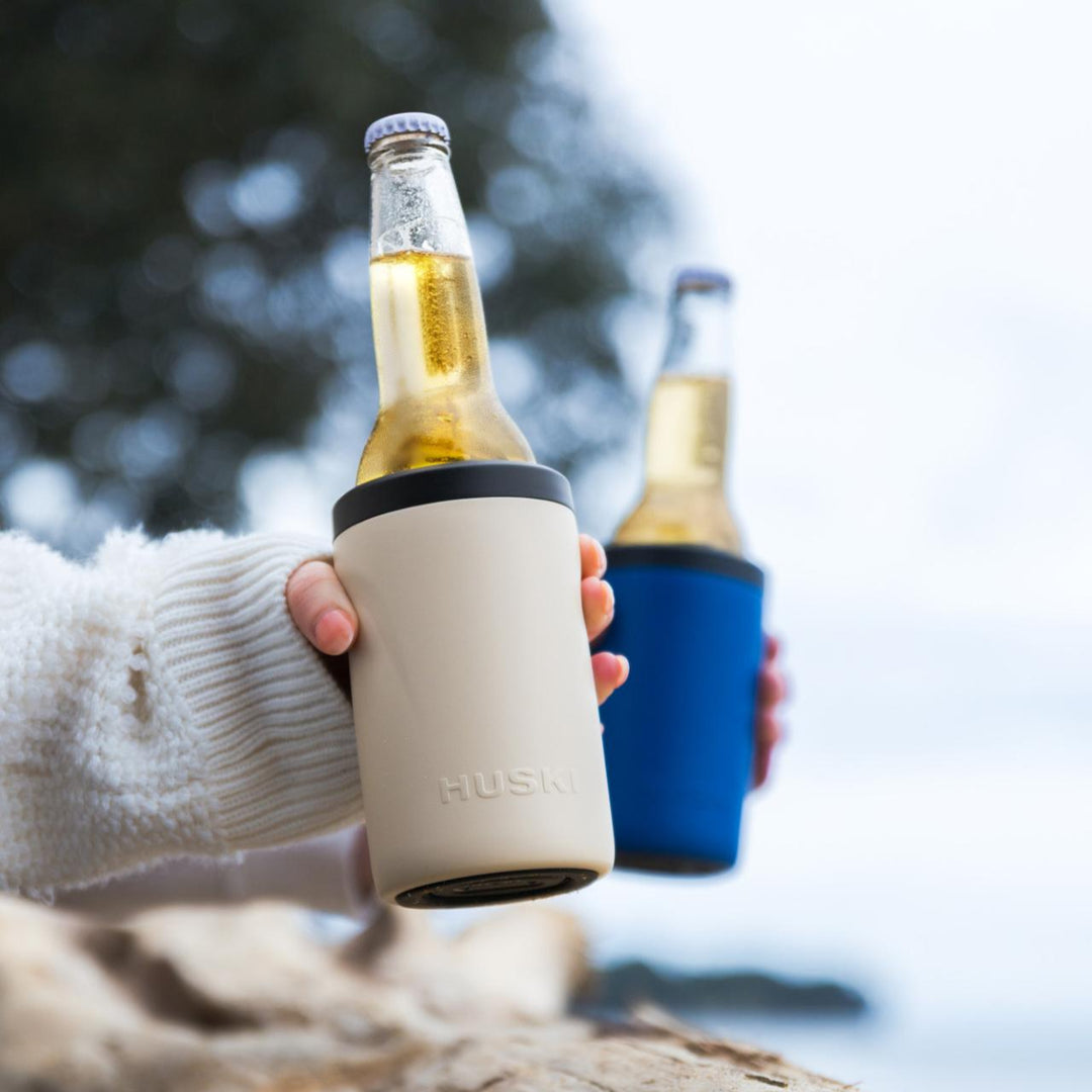 Two bottles of beer with Husky coolers on a wooden surface outdoors.