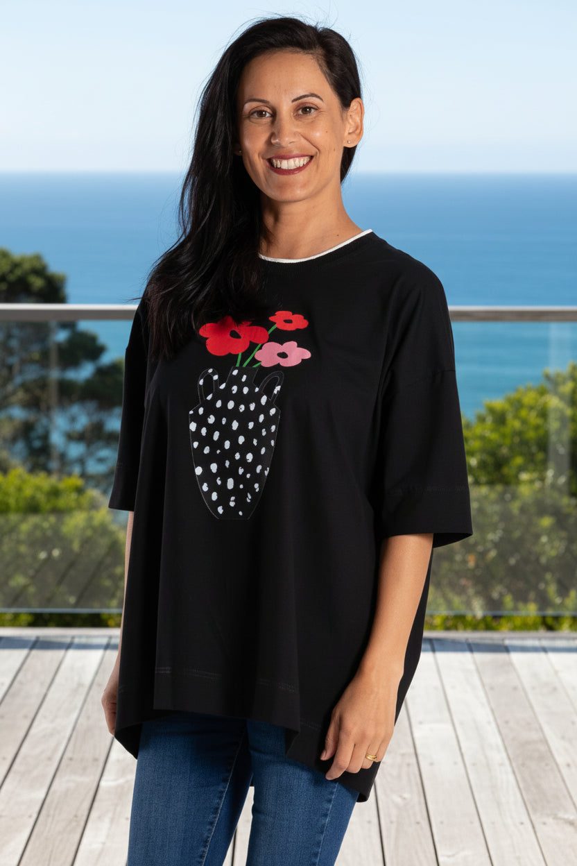 Woman wearing a black t-shirt with a graphic design, blue jeans, and white sneakers on a white background