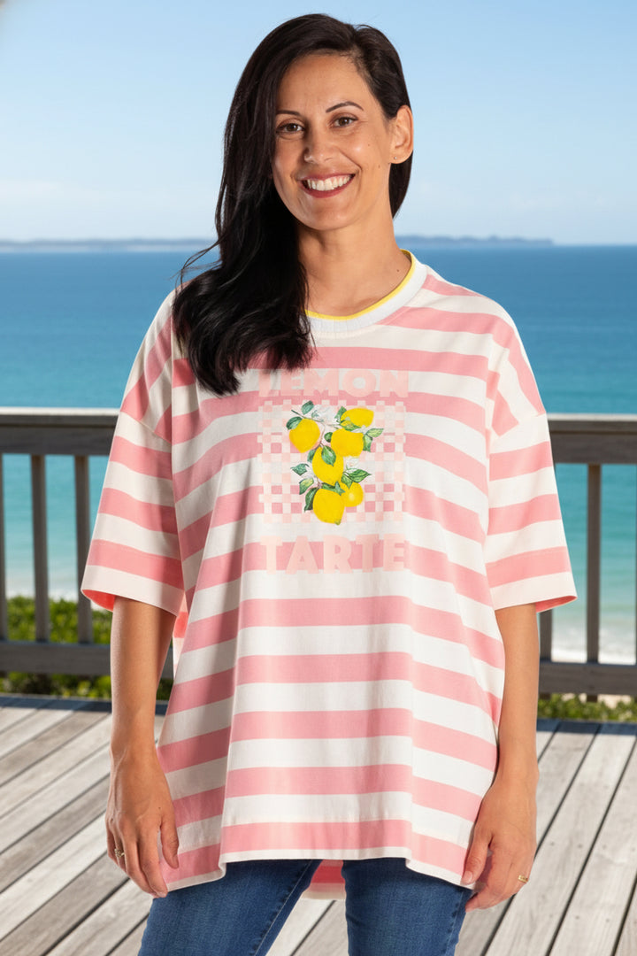 Woman wearing a pink and white striped shirt with a graphic design, blue jeans, and white sneakers on a white background