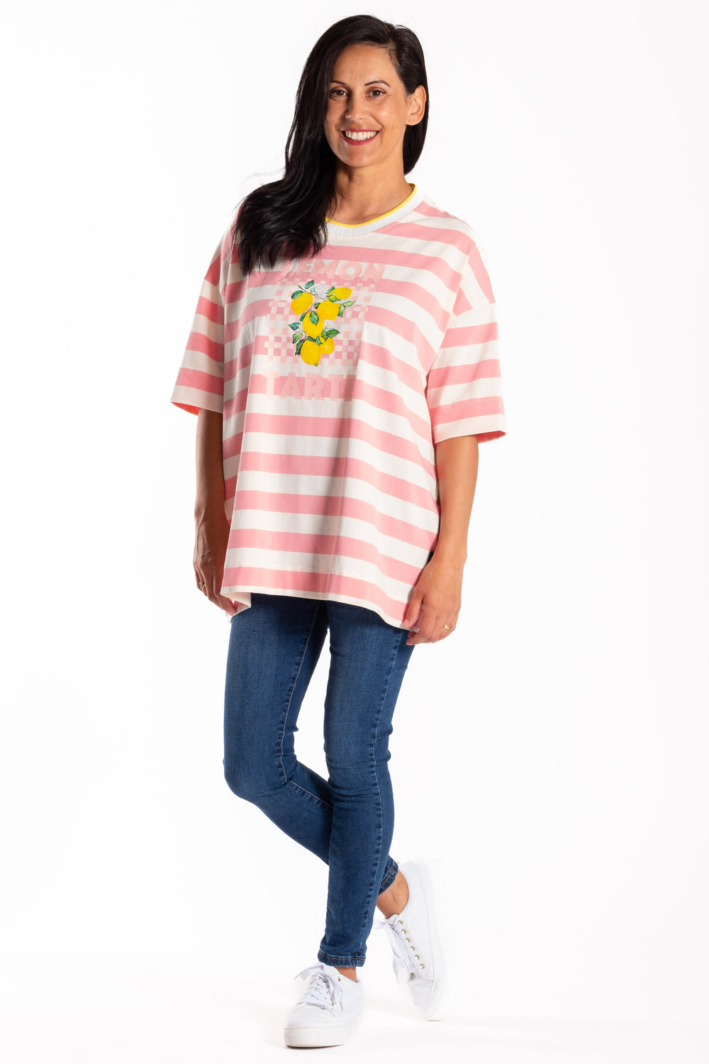 Woman wearing a pink and white striped shirt with a graphic design, blue jeans, and white sneakers on a white background