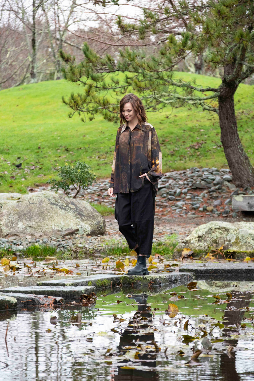 Woman standing by a pond in a park with trees and grass in the background