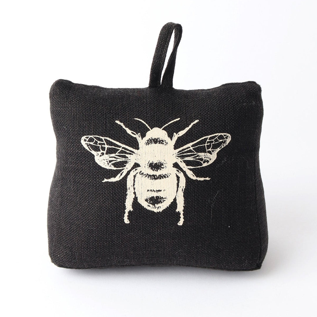 A square black fabric air freshener or sachet with a small loop at the top, featuring a white embroidered bee design on the front, set against a plain white background.