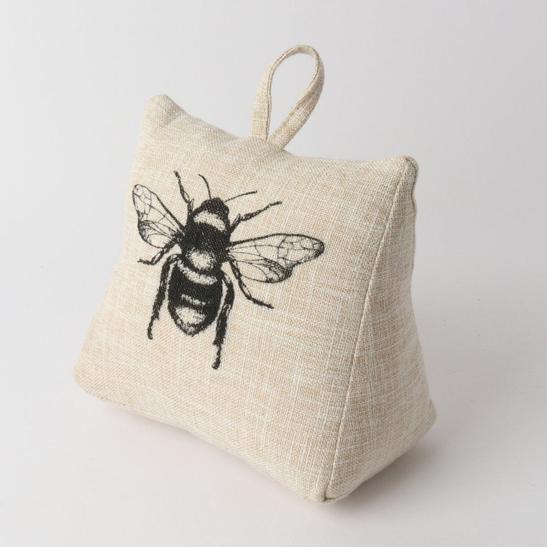 A small square beige linen pouch with a hanging loop, featuring a black embroidered bee design on the front, set against a plain light gray background.