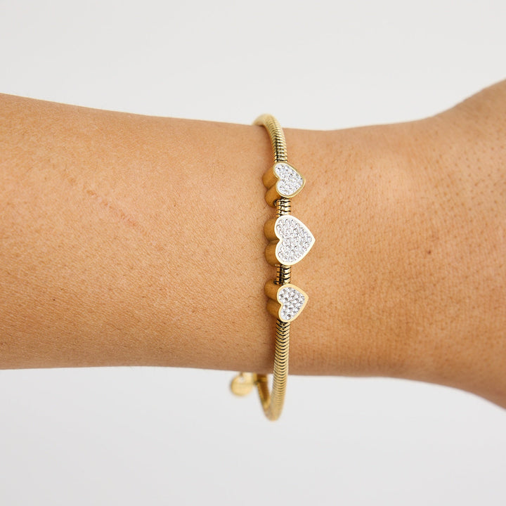 Gold bracelet with heart-shaped charms on a wrist against a light background