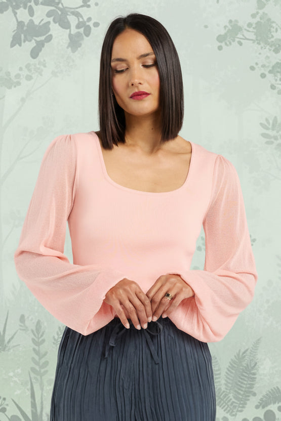 Woman wearing a pink blouse and dark pleated pants on a white background