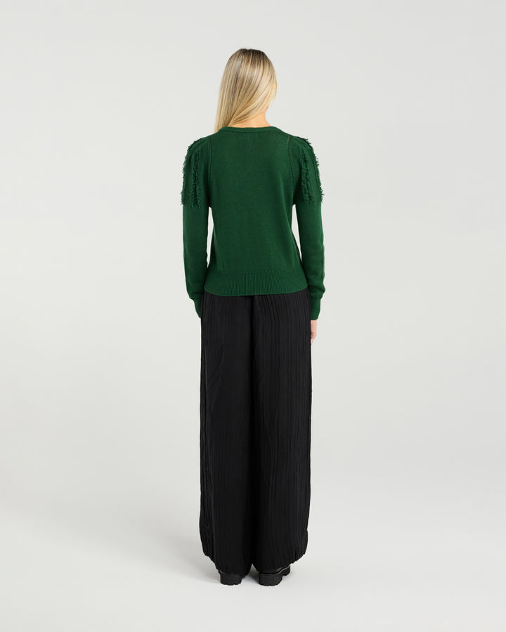 Woman wearing a green top and black pants on a white background