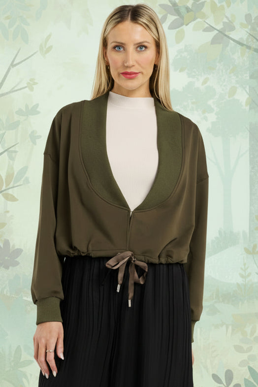 Woman wearing a green cardigan over a white turtleneck and black pants on a white background