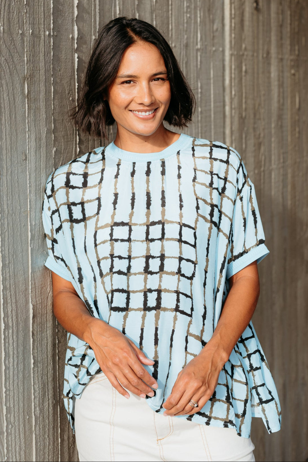Woman wearing a light blue patterned top against a wooden wall