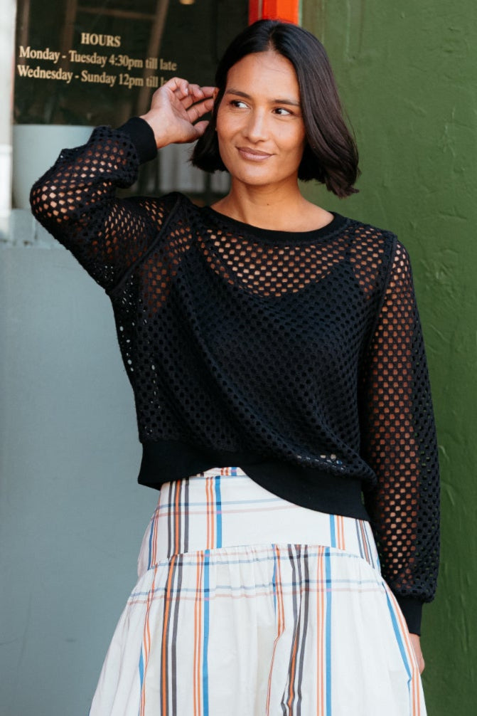 Woman in black top and plaid skirt standing in front of a green wall with glass doors.
