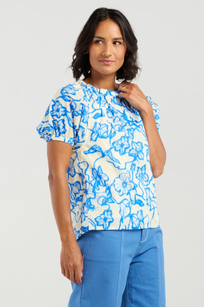 Woman wearing a blue and white floral top with wide-leg blue pants on a white background
