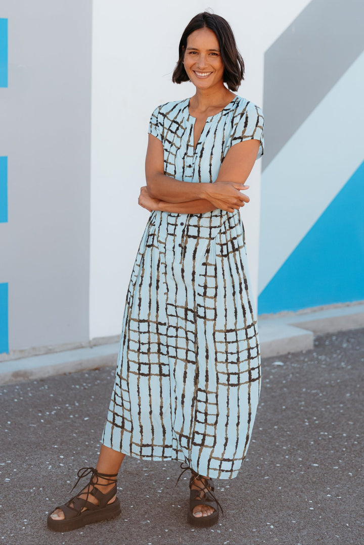 Woman in a checkered dress standing against a colorful wall.