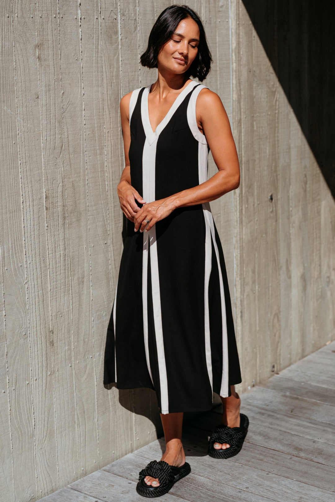 Woman wearing a black and white dress standing against a concrete wall.