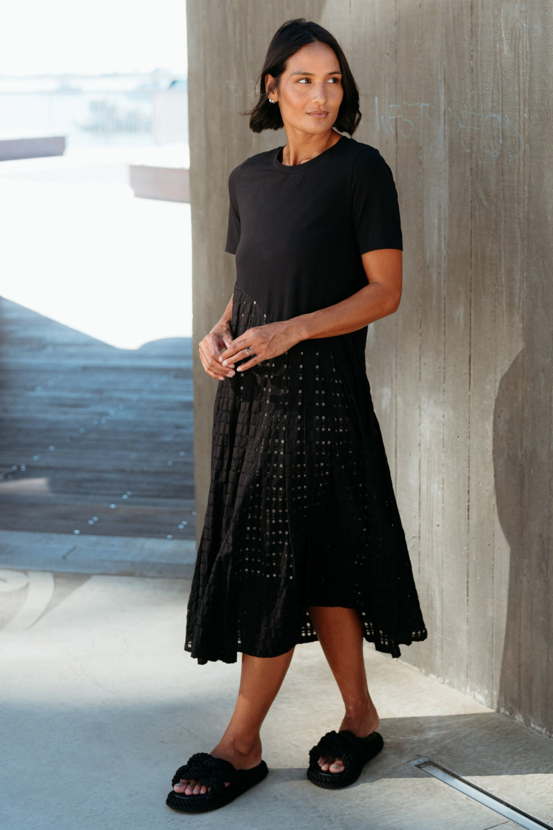 Woman in a black dress standing against a concrete wall.