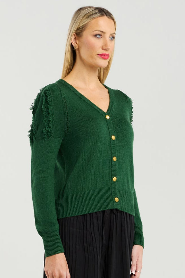 Woman wearing a green cardigan with gold buttons and black pleated pants on a white background