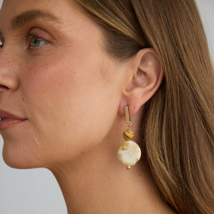 Close-up of a woman wearing gold earrings with a white pearl on a neutral background