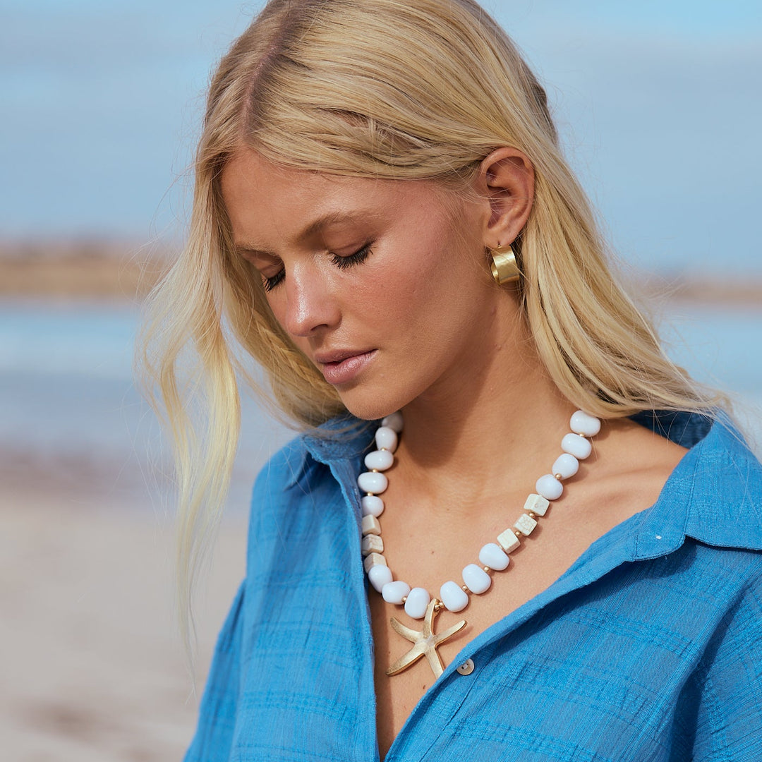 Woman wearing a blue shirt and pearl necklace on a beach