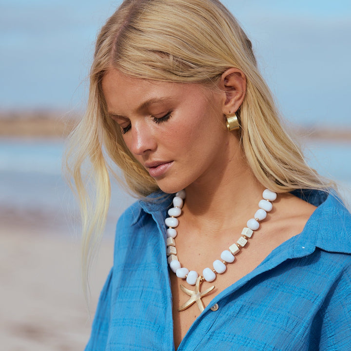 Woman wearing a blue shirt and pearl necklace on a beach