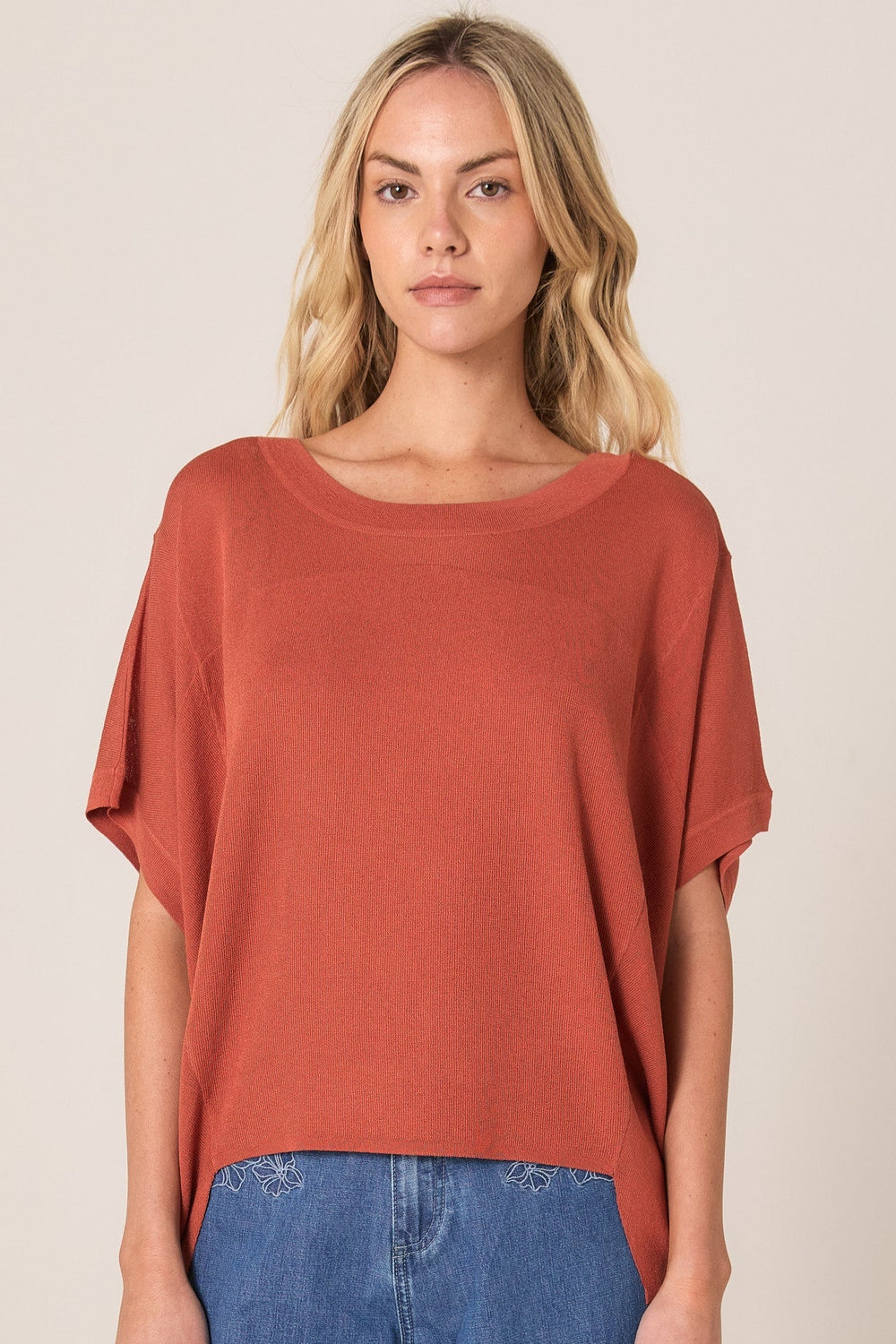 Woman wearing a rust-colored FATE & BECKER ESTHER top and blue jeans on a beige background