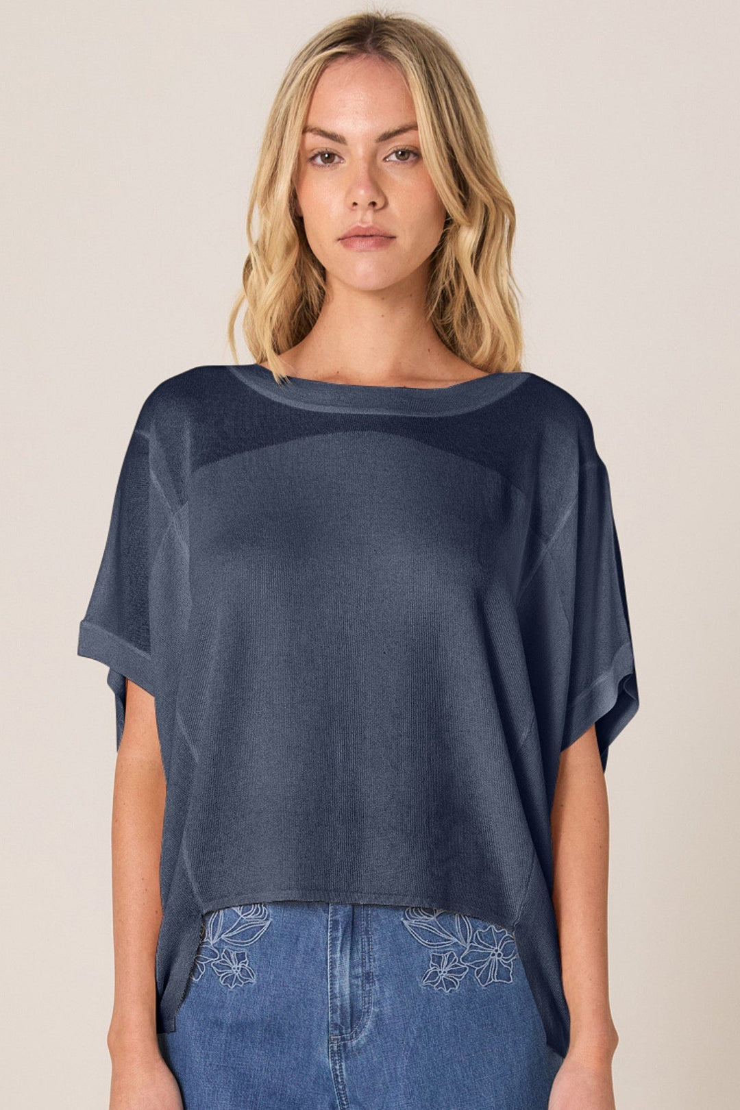 Woman wearing a dark blue FATE & BECKER KNIT top and jeans on a beige background