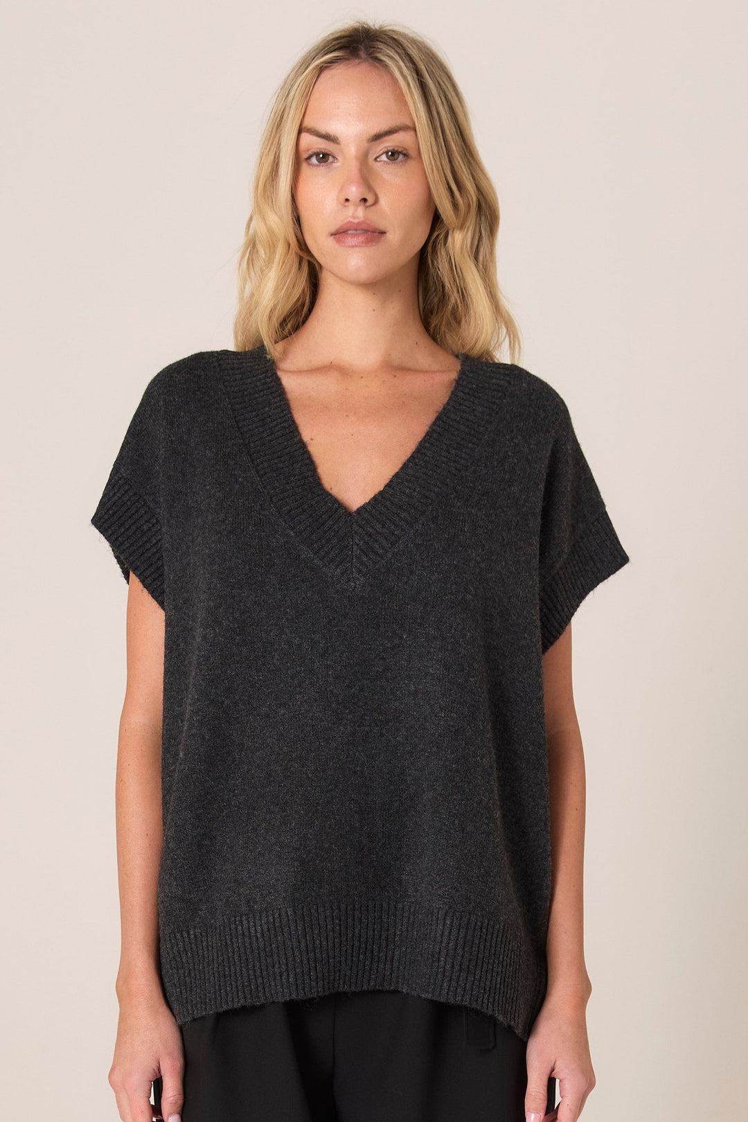 Woman wearing a dark gray FATE & BECKER RAE VEST knit top against a beige background