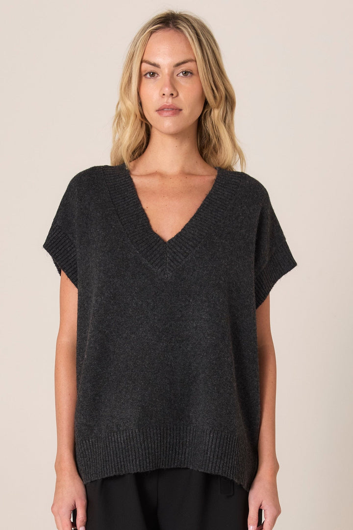 Woman wearing a dark gray FATE & BECKER RAE VEST knit top against a beige background