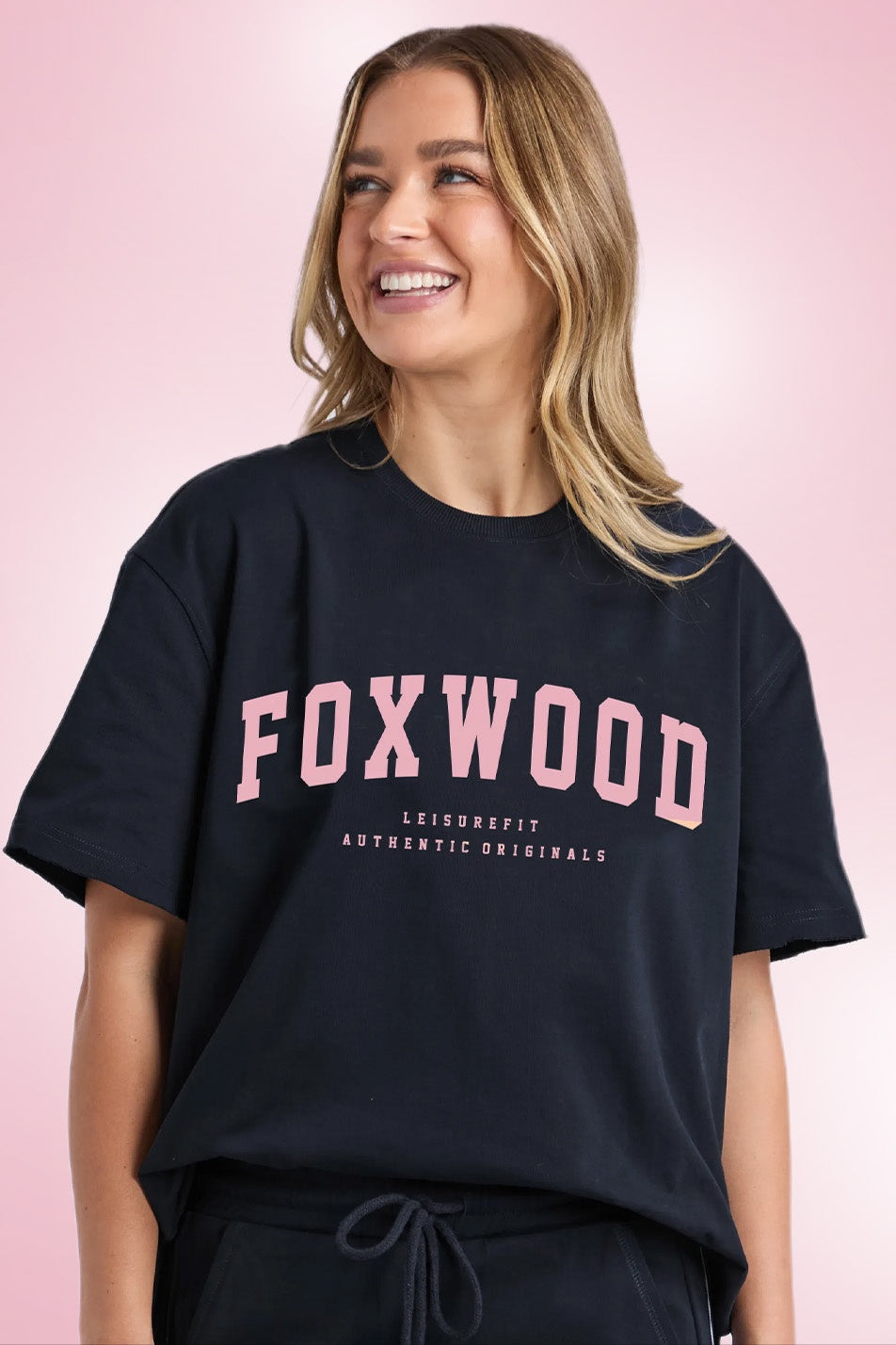 Woman wearing a black t-shirt with 'FOXWOOD' printed in pink on a pink background