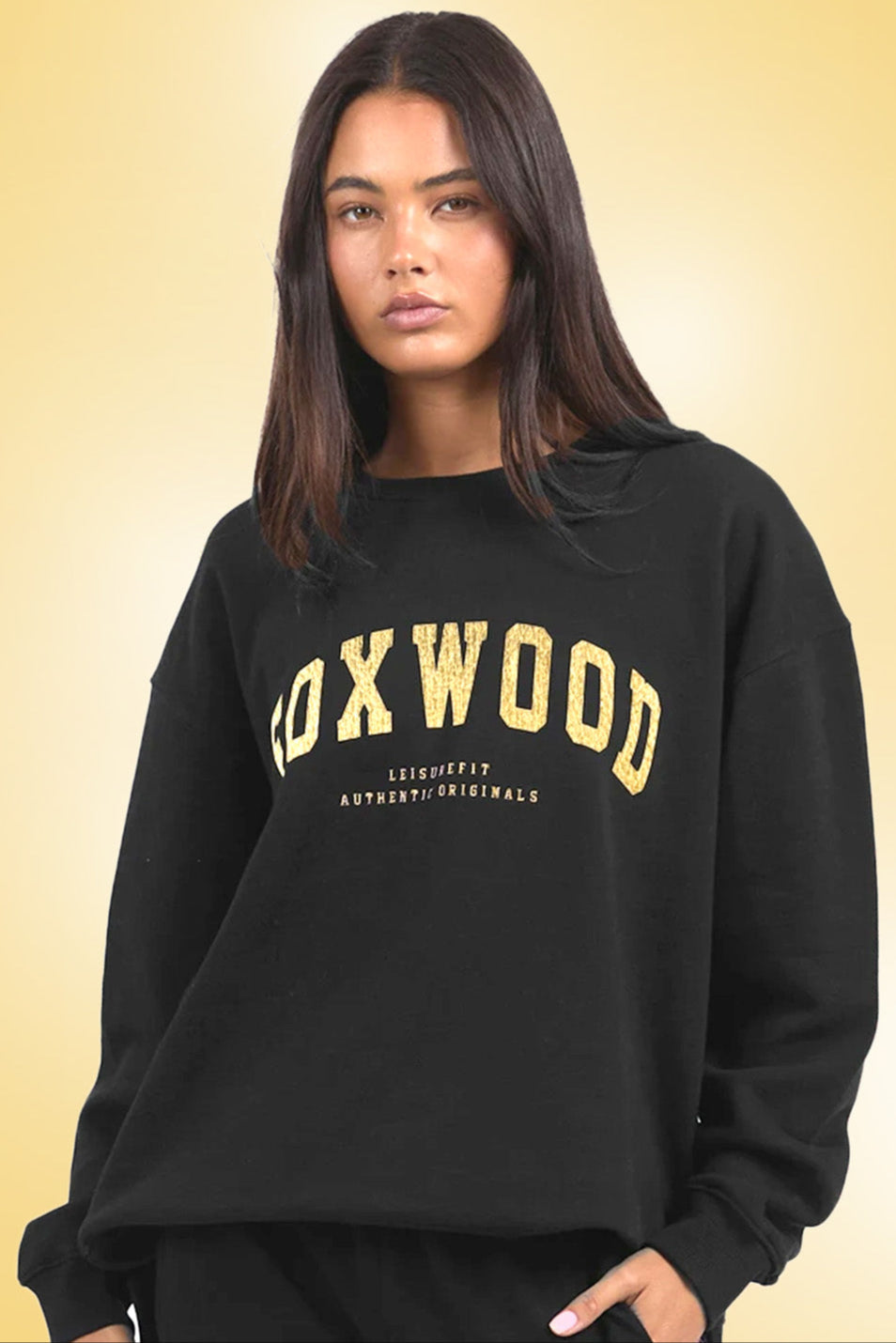 Woman wearing a black sweatshirt with 'FOXWOOD' printed on it against a beige background