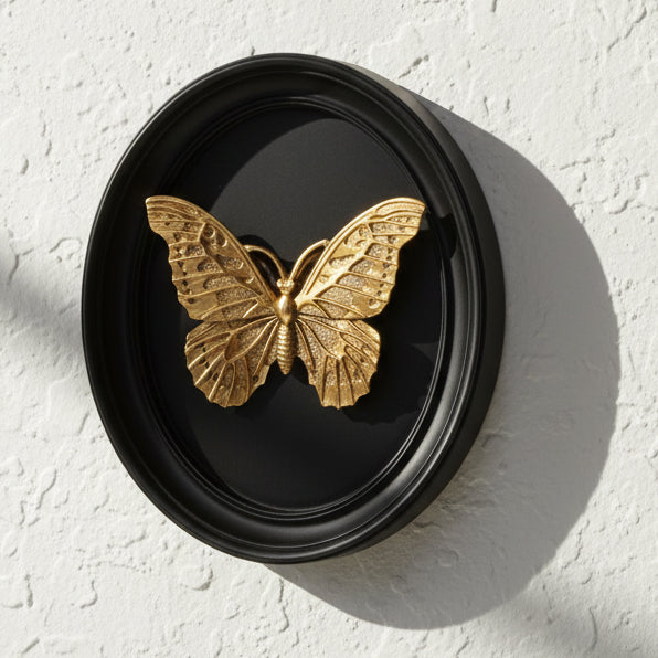 Gold butterfly decorative item in a black oval frame on a white background