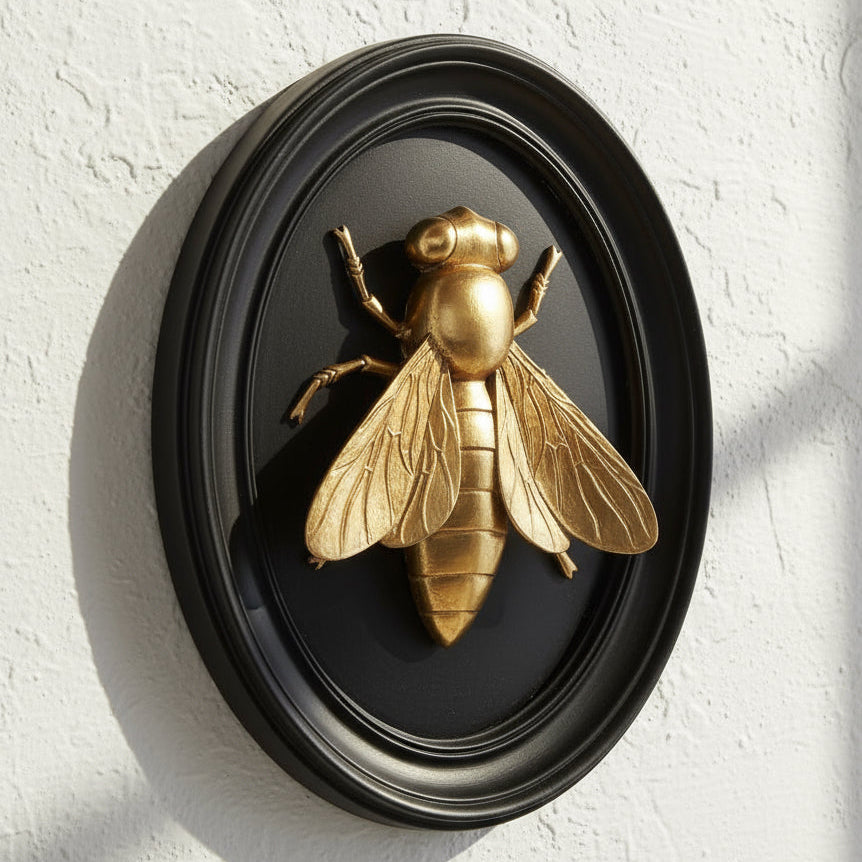 Gold bee sculpture in a black oval frame on a white background