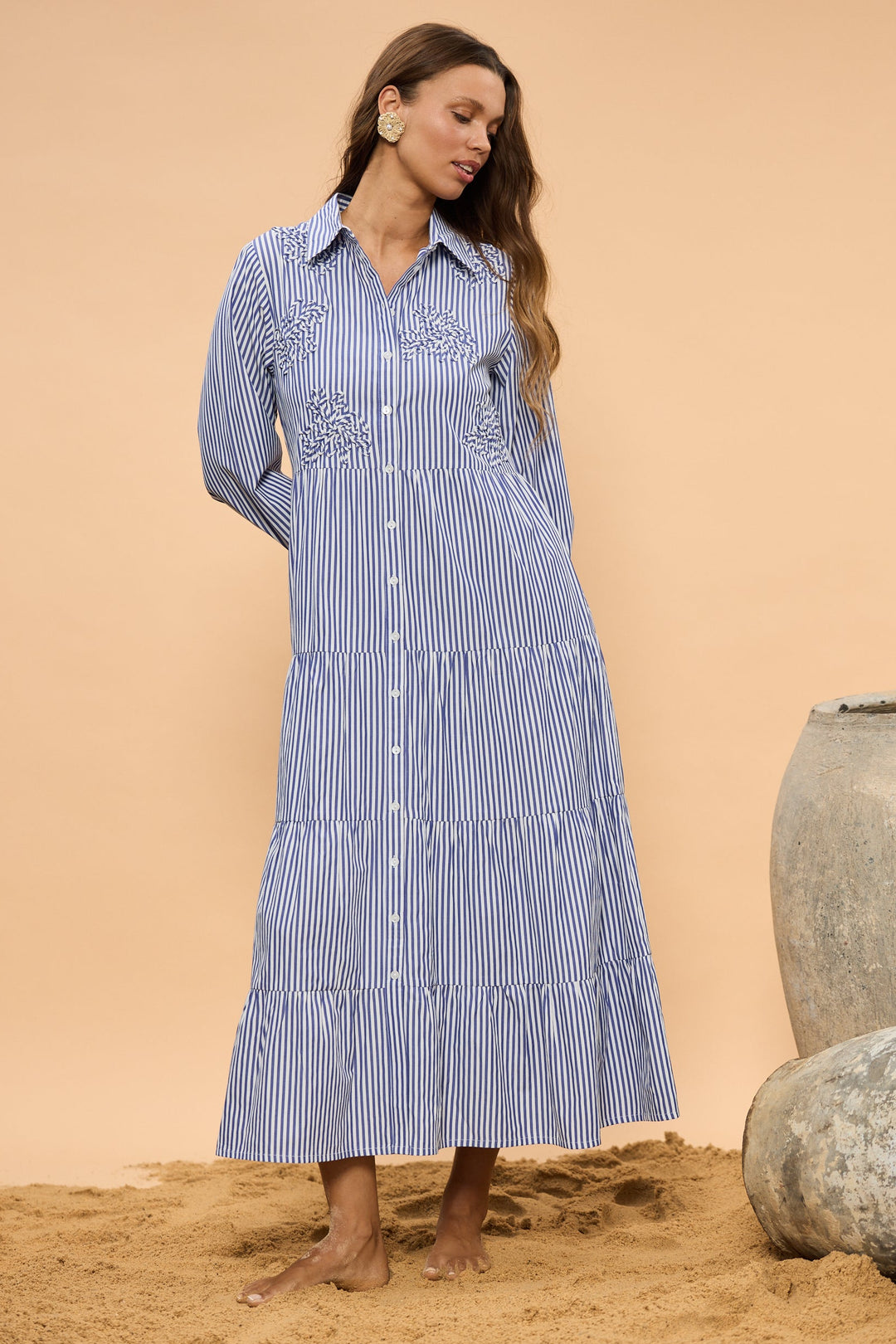Woman wearing a blue and white striped dress standing on sand with a beige background