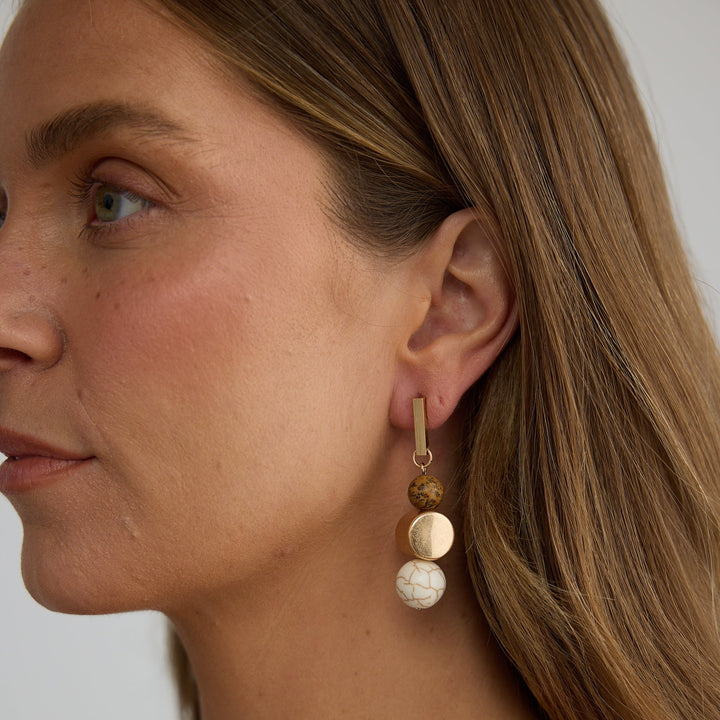 Close-up of a woman wearing a gold and pearl earring against a neutral background