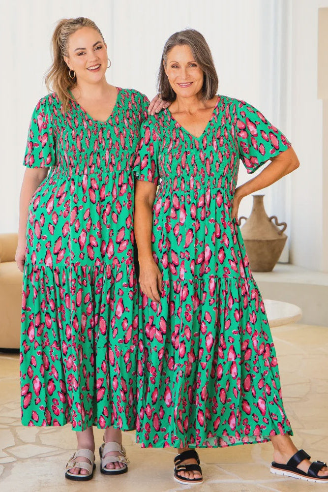 Two women wearing green dresses with pink patterns in a living room setting.