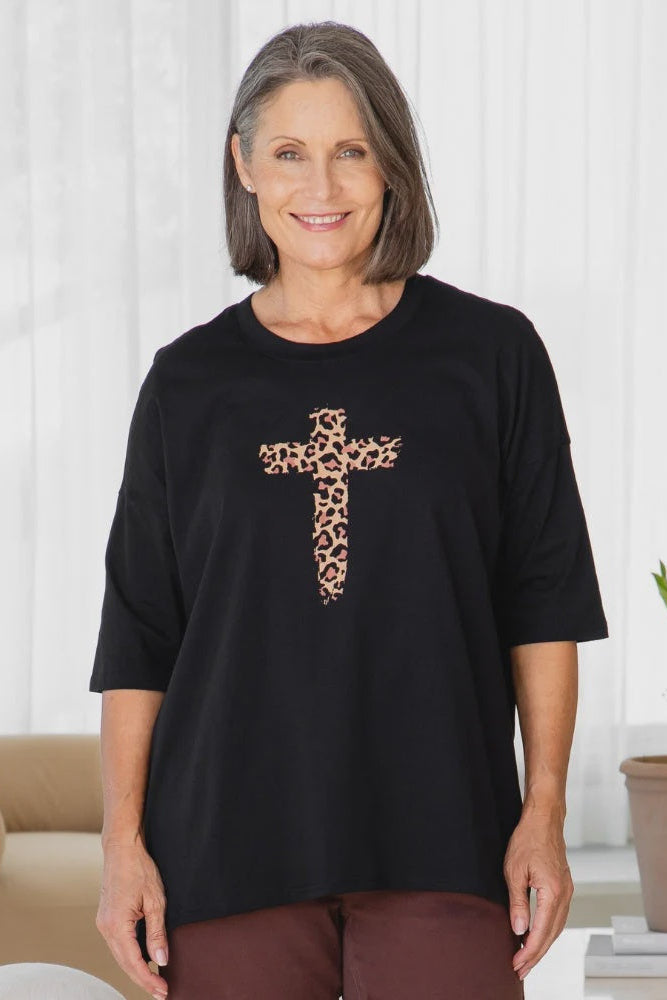Woman wearing a black t-shirt with a leopard print cross design in a living room setting.
