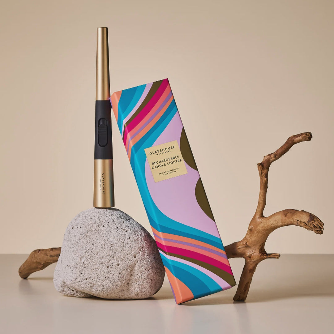 Colorful striped product packaging of a glasshouse usb rechargeable candle lighter leaning against a rock with a beige background