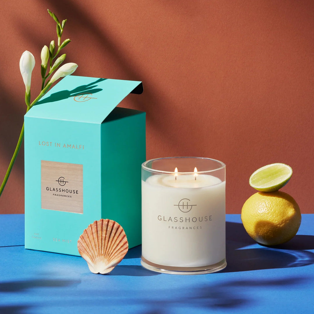 Glasshouse candle with packaging, lemon, and shell on a blue surface with a brown background