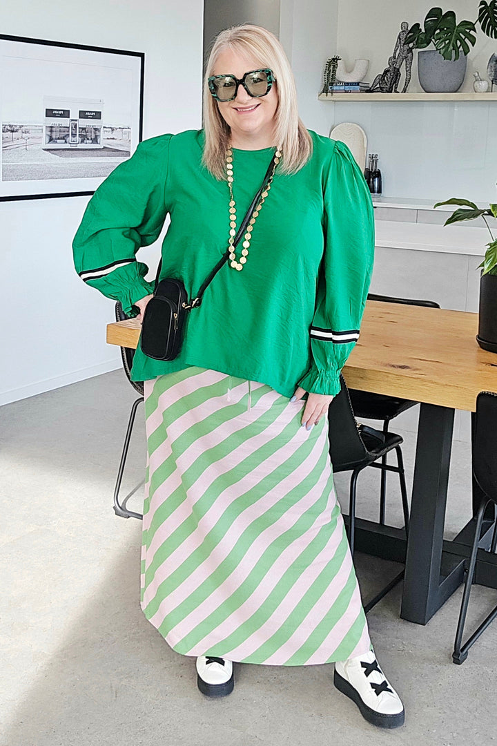 Woman in green top and striped skirt standing in a modern office setting.