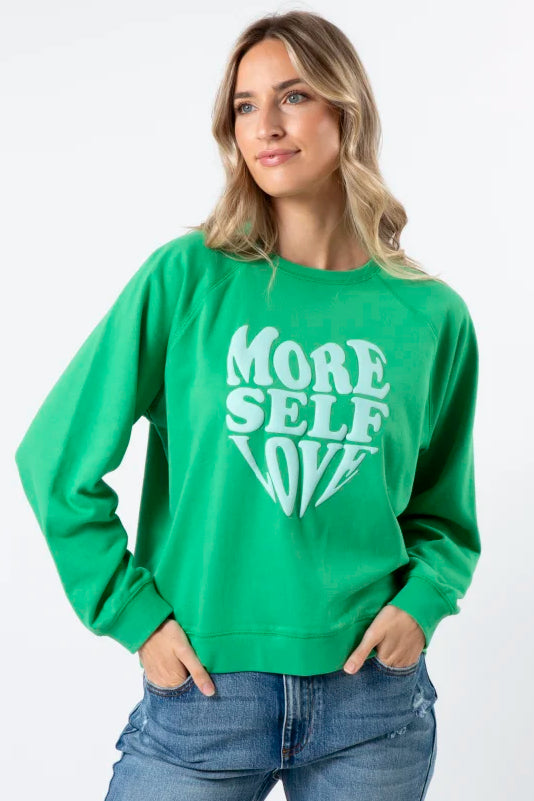 Woman wearing a green sweatshirt with 'More Self Love' text on a white background